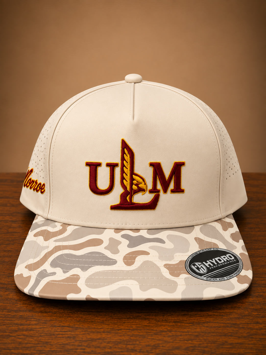 Duck marsh camo brim cap with ULM embroidery on front and Monroe script embroidery on the side.