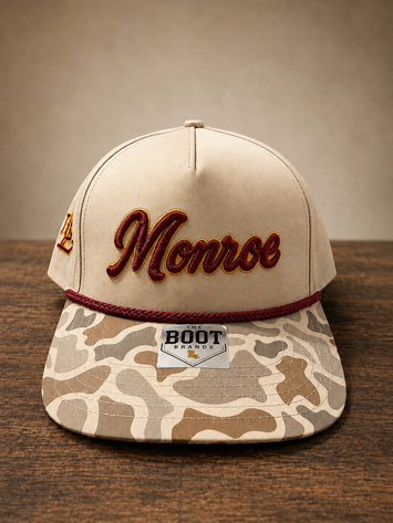 Duck marsh camo brim cap with Monroe script embroidery on front and ULM embroidery on the side.